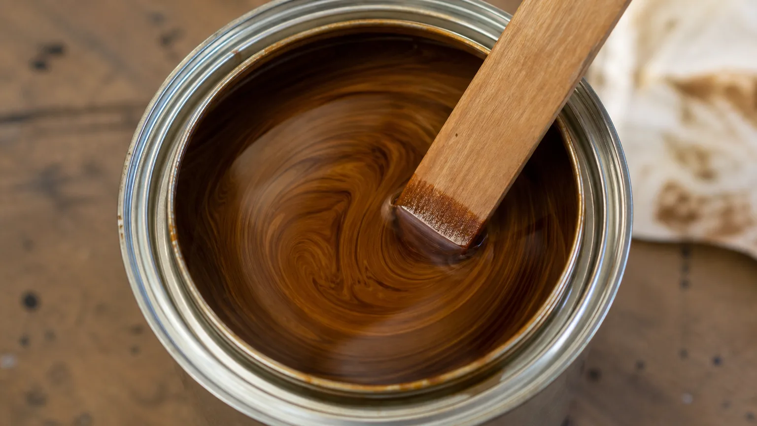 Hand stirring open can of brown wood primer with a wooden stir-stick