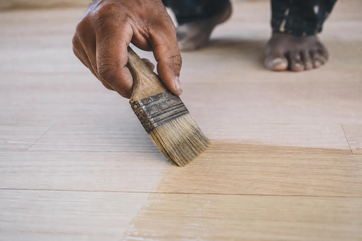 Indian craftsman brushing a thin first coat of clear penetrating oil into bare pale maple floorboards