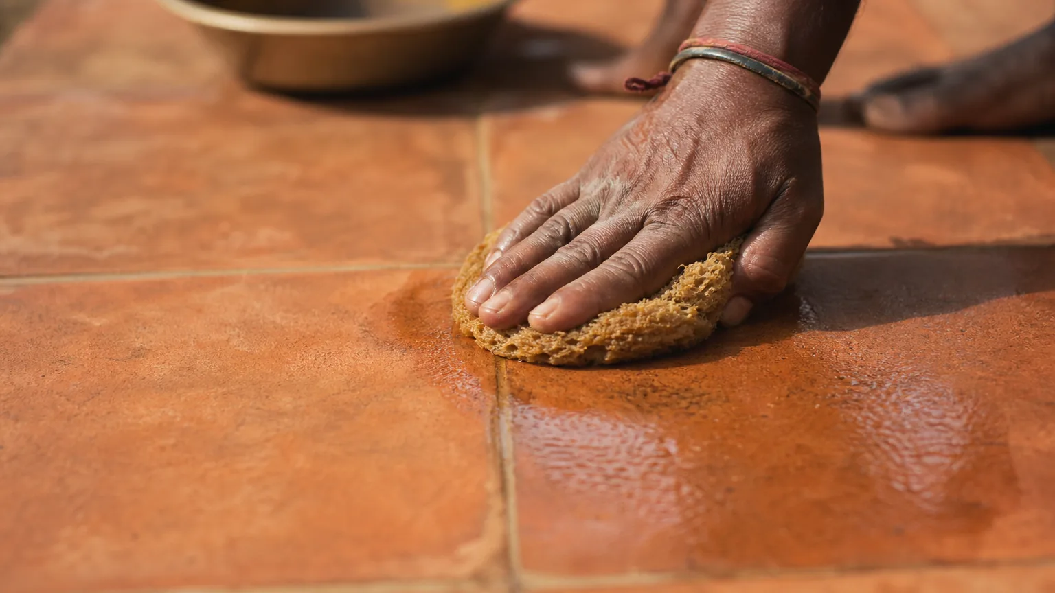 Indian craftsman applying second thin coat of stone and concrete oil to terracotta floor next day