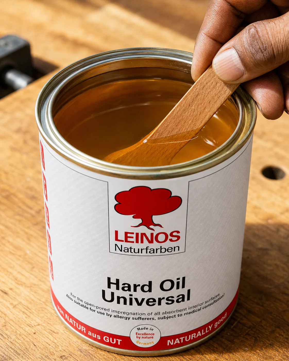Indian craftsman stirring an open branded LEINOS tin of warm amber natural wood oil with a wooden stick