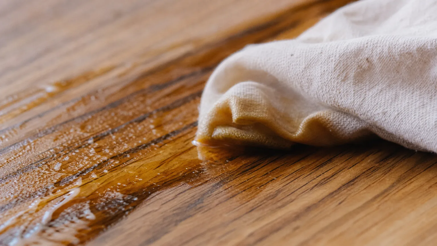 Cloth wiping LEINOS 280 across an oak worktop, oil pooling in the grain
