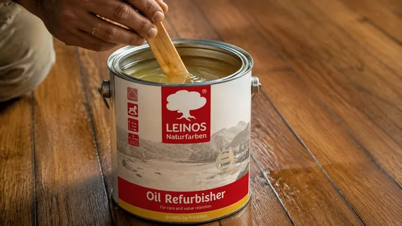 A craftsman stirring pale care oil in an open LEINOS Oil Refurbisher tin with a flat wooden stick