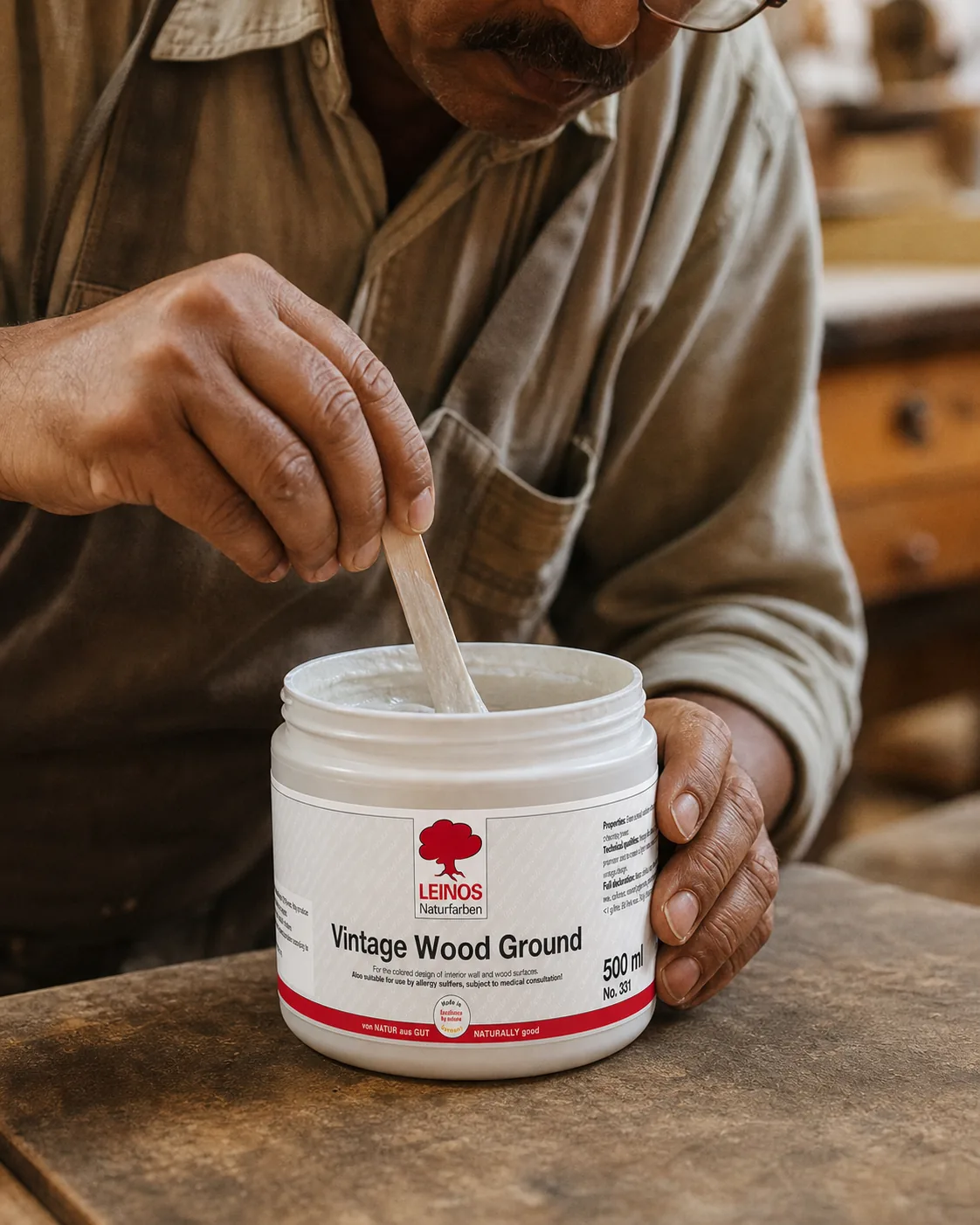 Stirring the matt-white Vintage Wood Ground paste inside the branded LEINOS 331 tub with a wooden stick