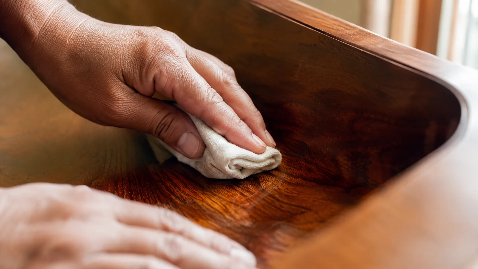 Hands buffing a freshly wax-glazed wood surface with a folded cotton cloth to a satin sheen