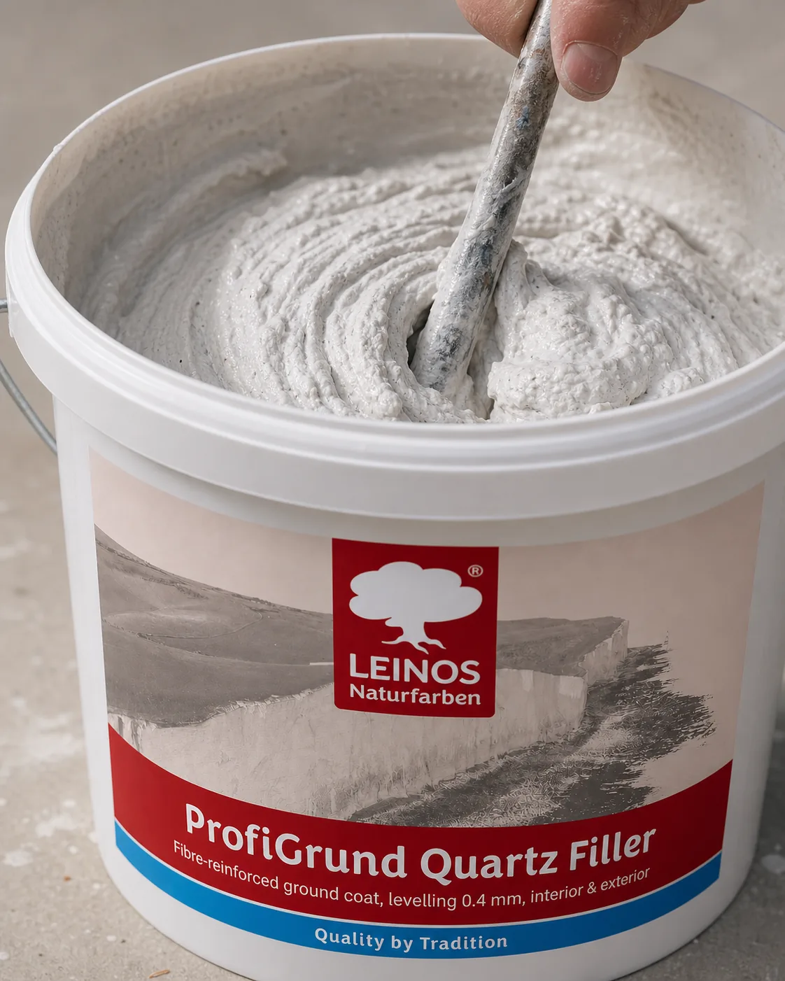 Open branded white LEINOS ProfiGrund Quartz Filler bucket with a paddle lifting thick pale grey-white quartz filler paste