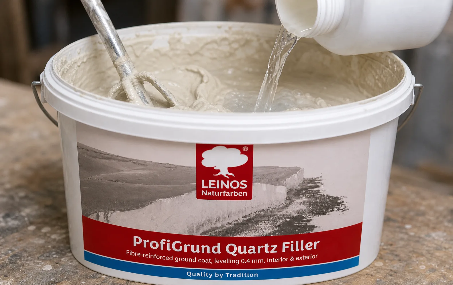 Pouring clear Profi-Fixativ from a small canister into the branded LEINOS ProfiGrund bucket to thin the quartz paste