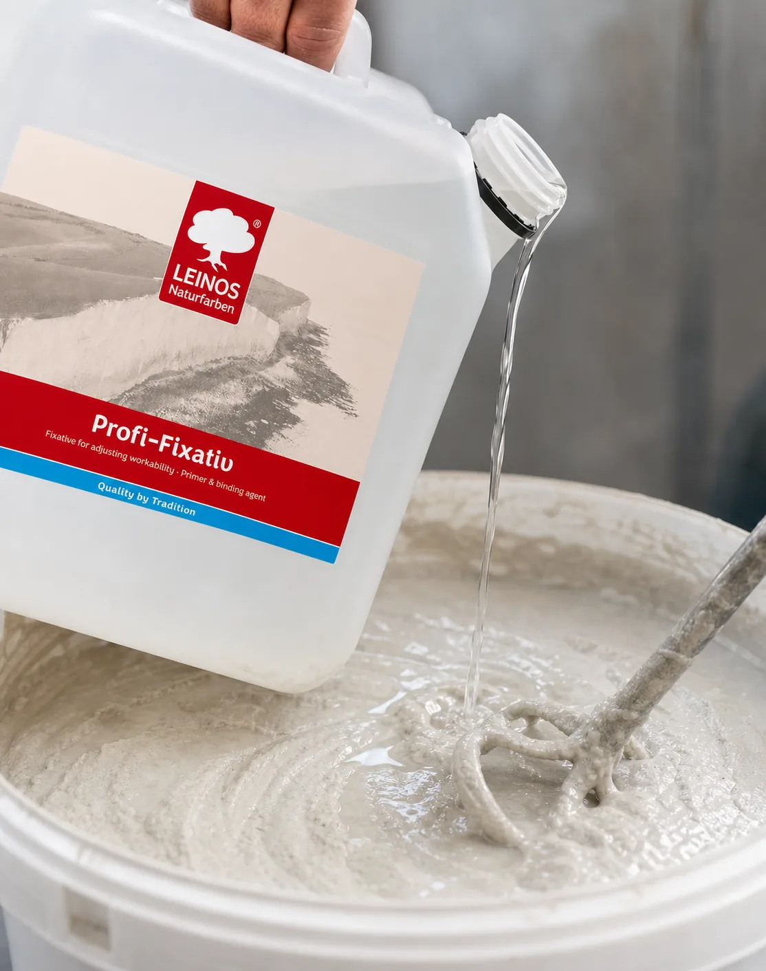 Pouring clear Profi-Fixativ from the branded LEINOS white canister into an open bucket of pale grey-white quartz filler paste to thin it