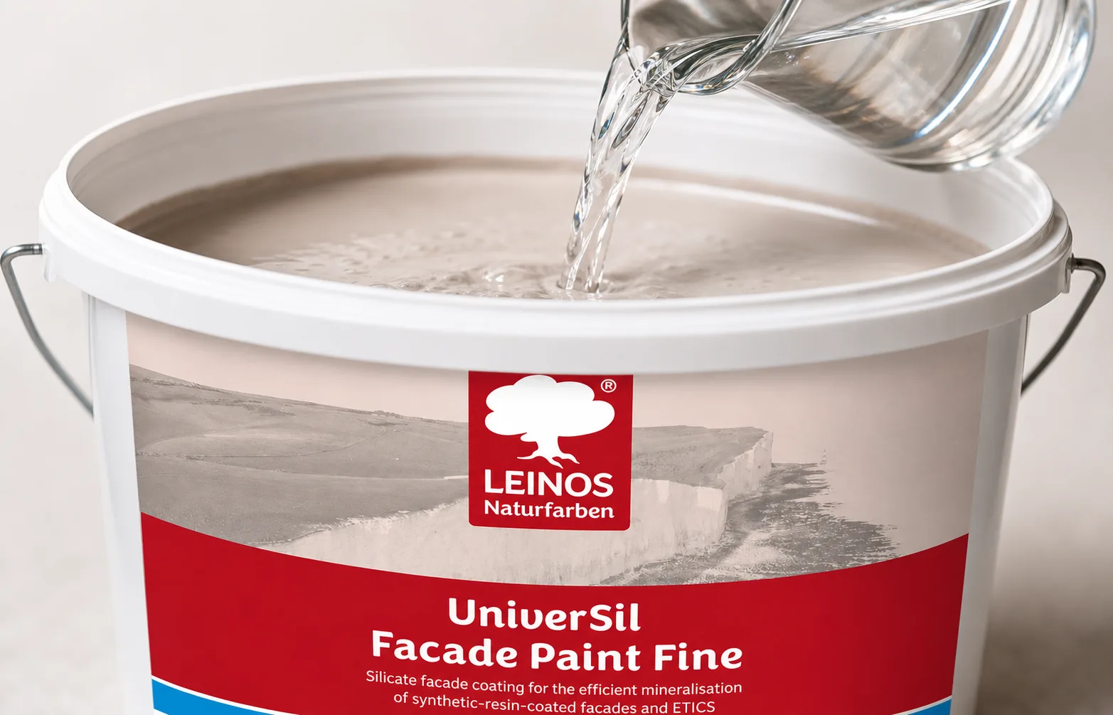 Pouring clean water from a jug into the branded LEINOS UniverSil Facade Paint Fine bucket to thin the mineral paint