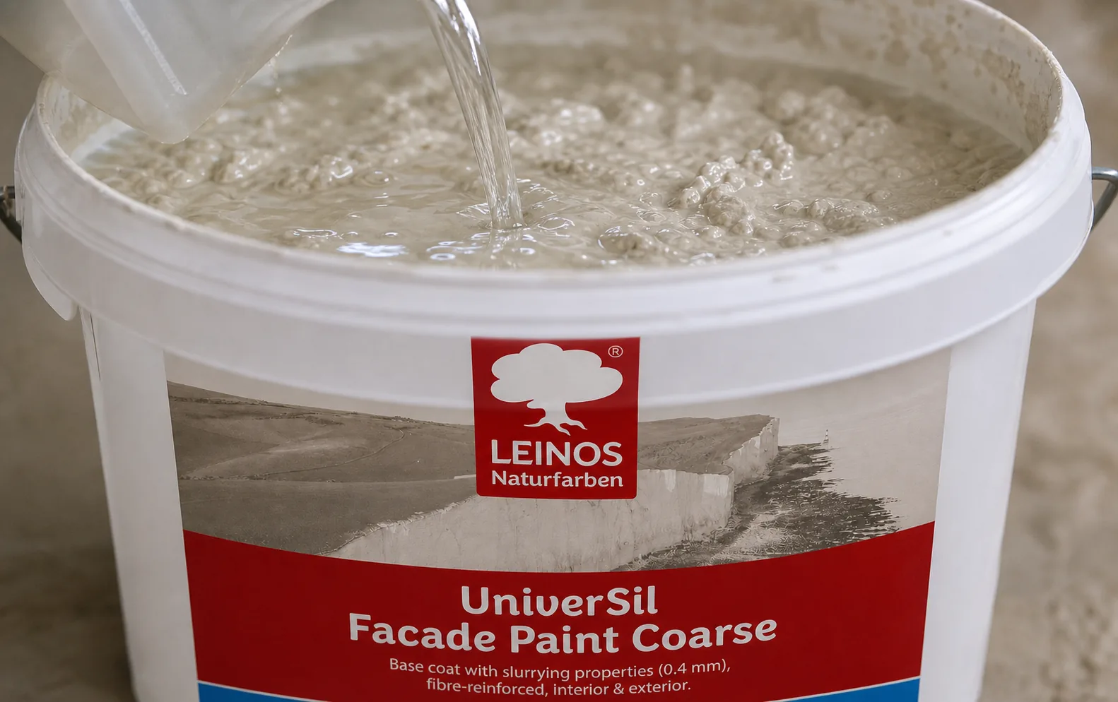 Pouring clear Profi-Fixativ from a canister into the branded LEINOS UniverSil Facade Paint Coarse bucket to thin the coarse mineral paste