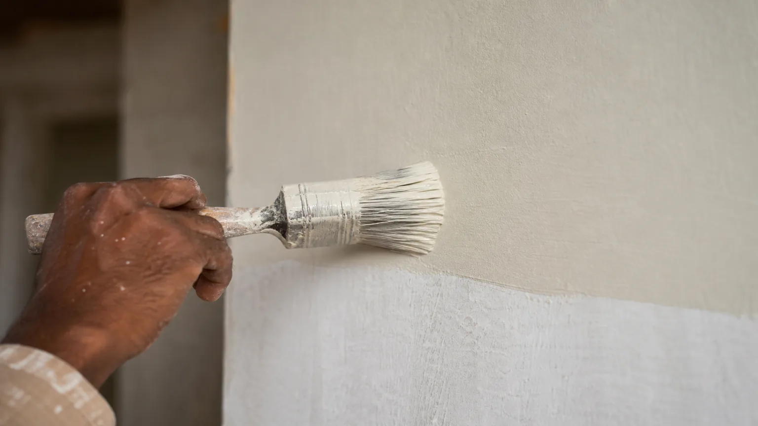 Indian craftsman applying matt lime paint with a brush over the primed wall, fresh topcoat going on uniformly with no patchiness
