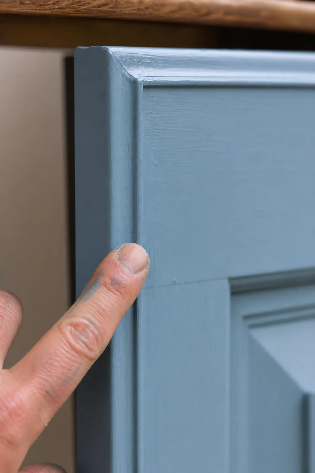 A wooden cabinet door freshly painted in soft matt Pacific-blue chalk paint drying, a craftsman fingertip lightly touching the corner to check it is touch-dry
