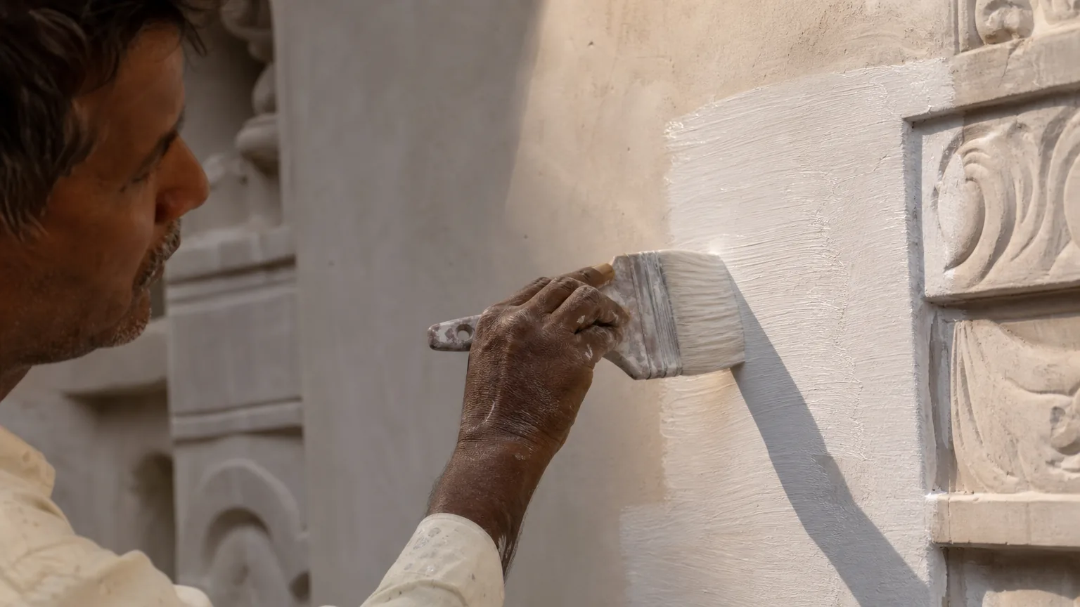 Indian craftsman applying the second coat of lime paint over the dried first coat with a wide masonry brush — deeper opacity visible