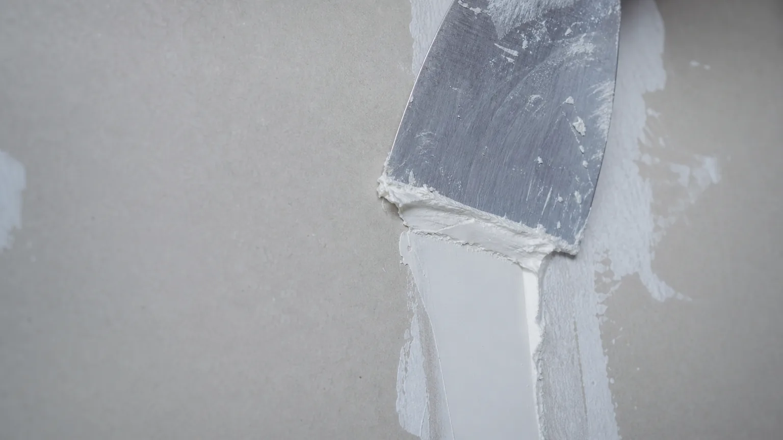 Close-up of an Indian plasterer pressing LEINOS 684 filler firmly into a plasterboard joint with a putty knife and pulling it flat