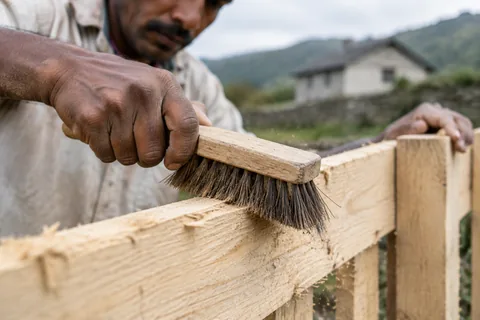 A craftsman brushing loose fibres off an untreated rough-sawn fence board before painting