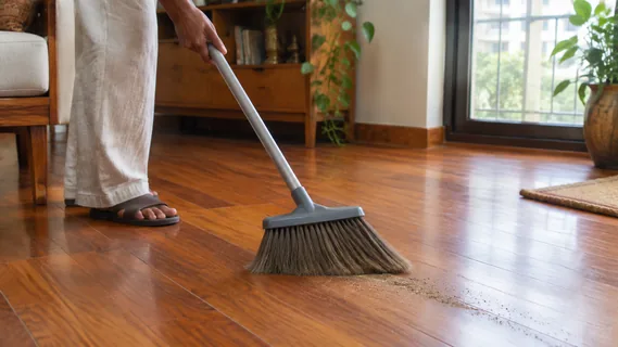 A soft broom sweeping fine grit along the grain of an oiled teak floor before it is washed