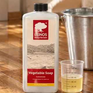 A LEINOS Vegetable Soap bottle beside a measuring cup holding about 40 ml of soap, a bucket of water behind