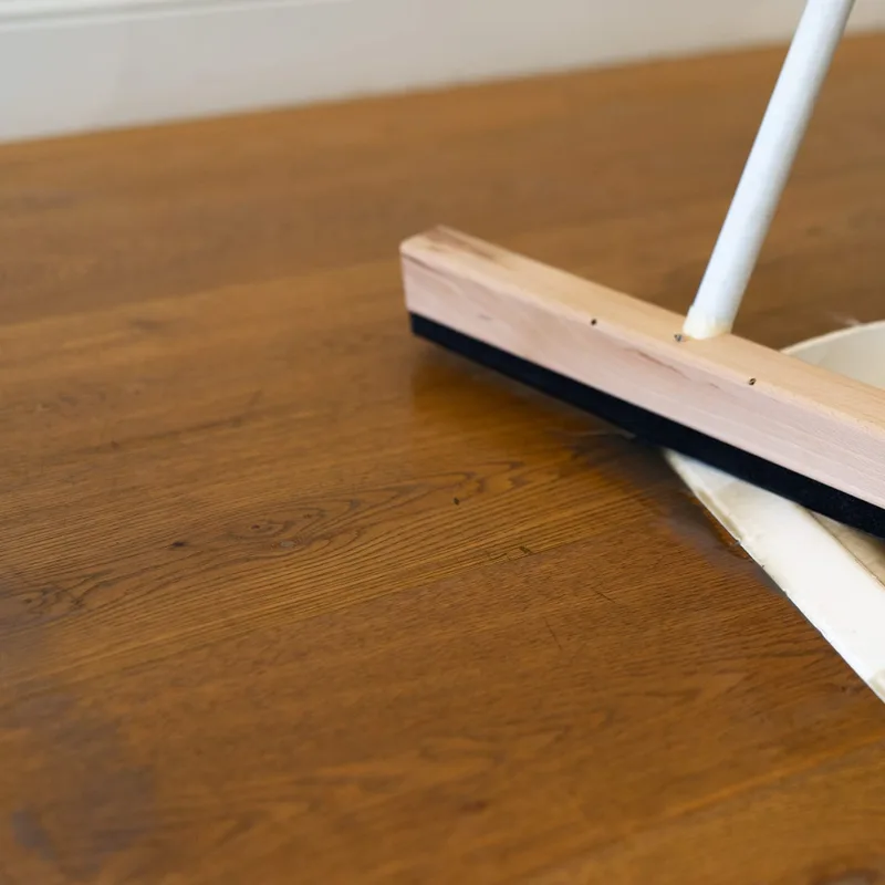 A wooden squeegee blade and a dustpan resting on an oiled timber floor