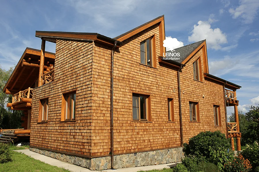 Stone-and-cedar transition at the foundation course — LEINOS Wood Varnish 260 protects the lowest shingle row without filming the timber surface.