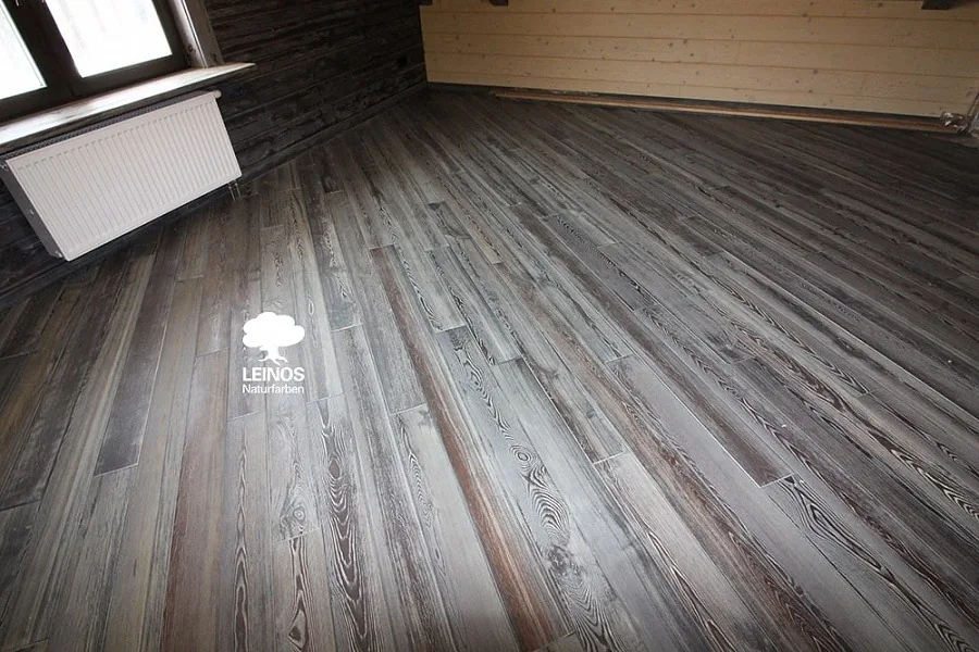 Floor-to-wall junction detail — uniform weathered-grey tone with no flashing where the floor planks meet the wall paneling.