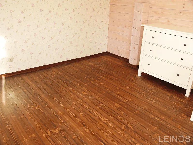 Wall-to-floor junction — clean tonal break between dark larch floor and light unfinished pine wall.
