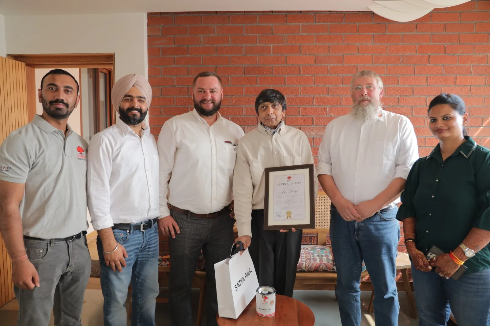 LEINOS India team with the Noida homeowner holding a framed LEINOS Appreciation certificate in the completed pine bedroom project — a tin of Interior Hardwax Oil 290 on the table.