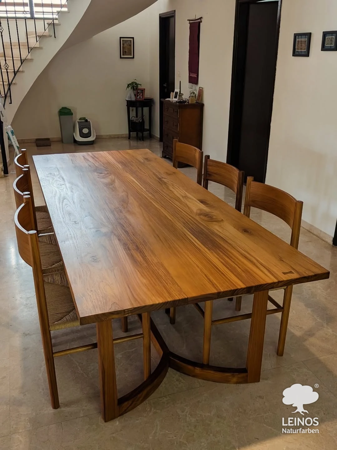 A bespoke solid teak dining table on a curved sculptural base with rush-seat chairs in a private Kochi home, finished in LEINOS Interior Hardwax Oil 290 — warm satin natural-wood tone.