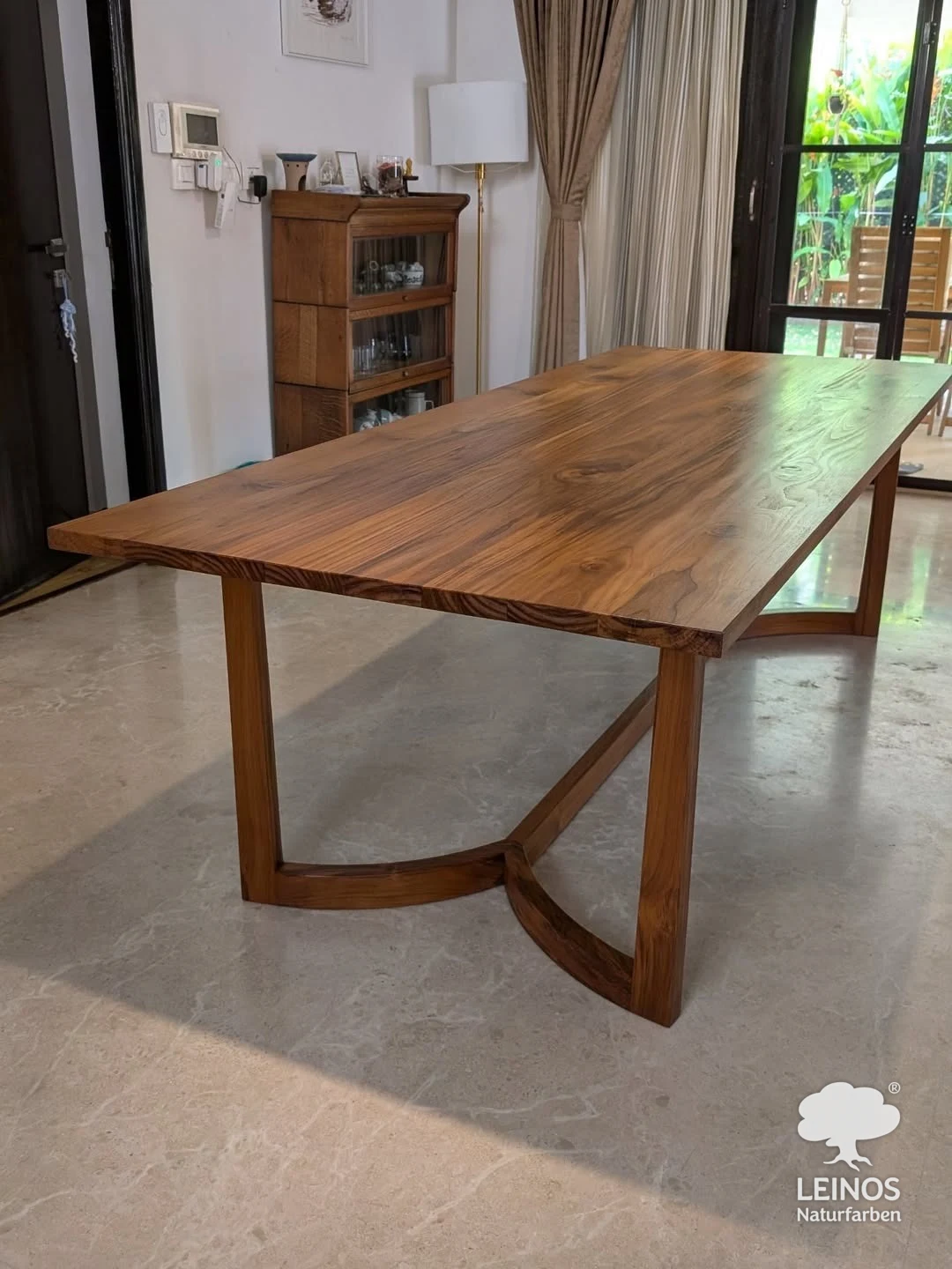 Solid teak dining table by a garden window in Kochi, Kerala — open-pore LEINOS Interior Hardwax Oil 290 finish showing the teak grain and a low satin sheen.