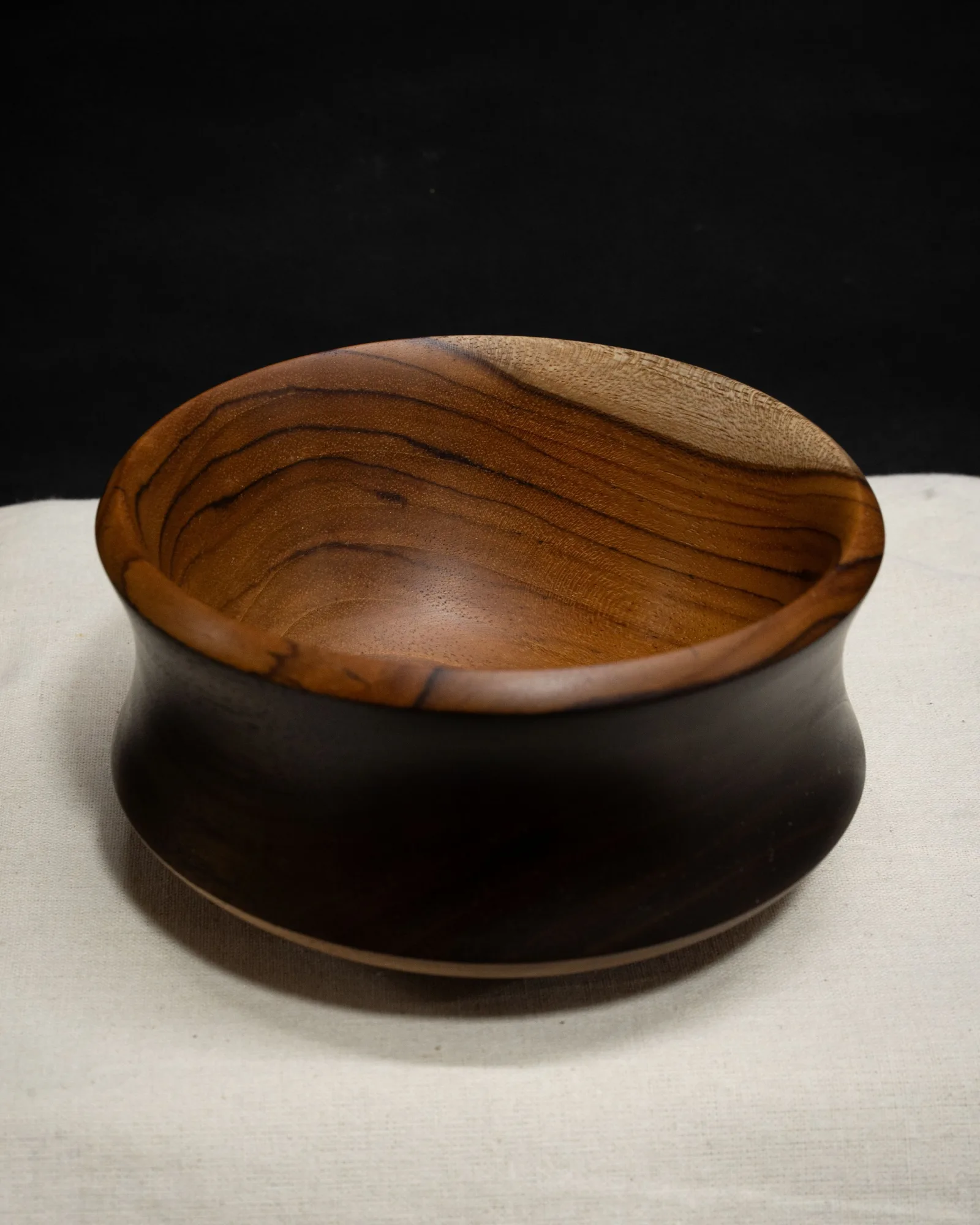 A footed turned teak bowl by Kathkani Studio with an ebonised exterior cove and warm natural interior, finished in LEINOS Interior Hardwax Oil 290.