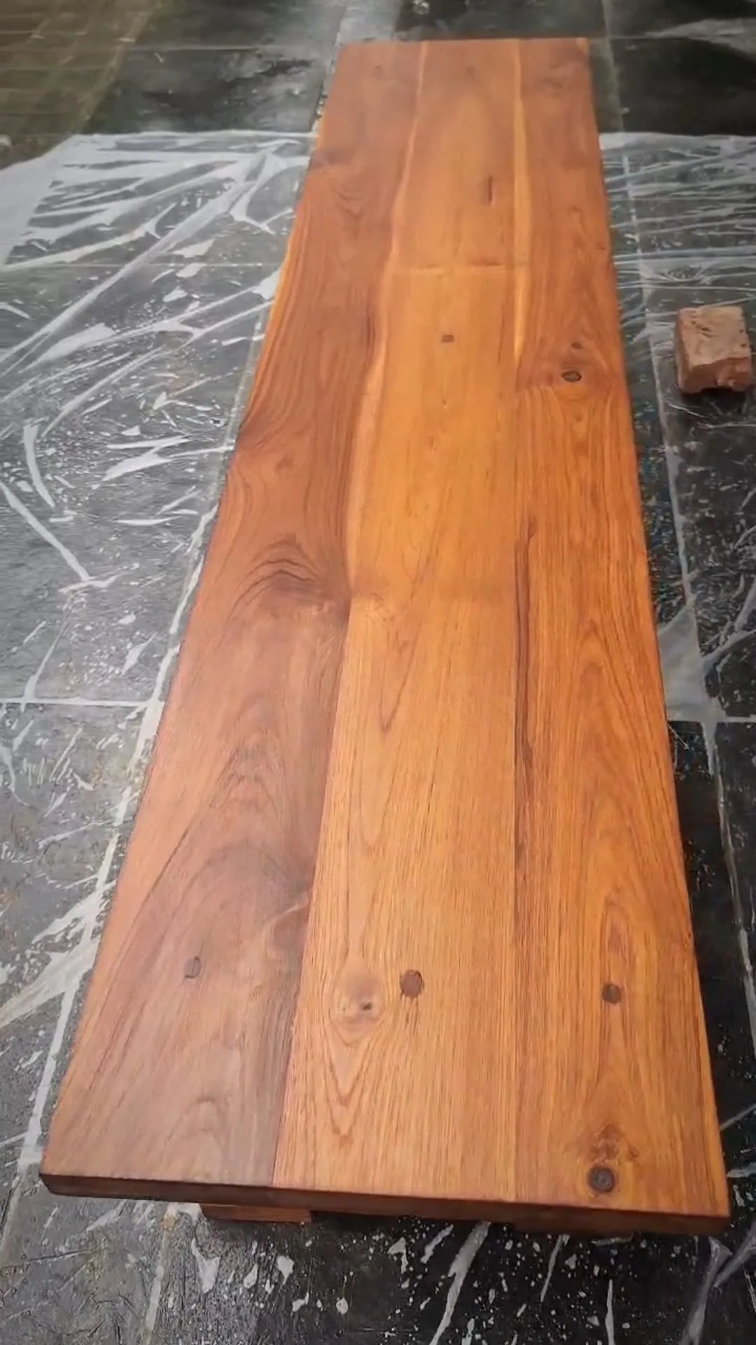 A LEINOS brand Reel of a solid-wood trestle table being hand-finished outdoors in Gurgaon with Premium Wood Varnish 260 in the Walnut shade. It follows the open-pore, oil-based varnish going onto the bare slab and the grain coming up to a warm walnut tone, with the brand's exterior-furniture claims (UV- and water-resistant, no peeling or cracking) shown on screen — a finishing showcase, not a full project walkthrough.