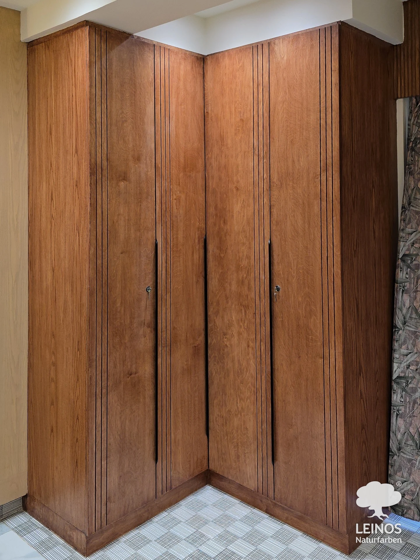 A corner run of fitted bedroom wardrobes in warm-toned wood, finished in Premium Hardwax Oil 290 with slim grooved detailing down the door edges.