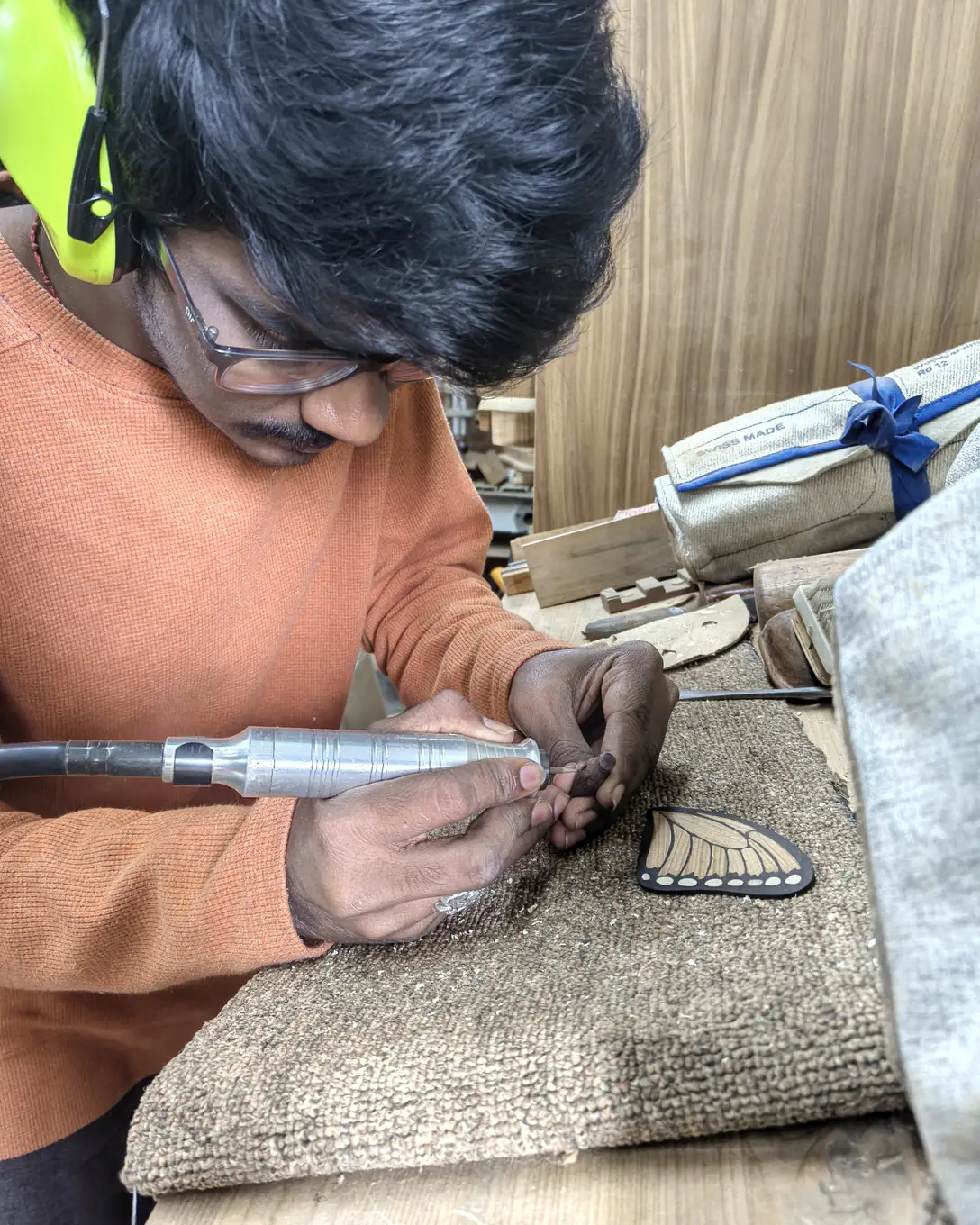 Hands guiding a rotary carving tool along a small wing resting on a sandbag, cutting the fine vein lines.