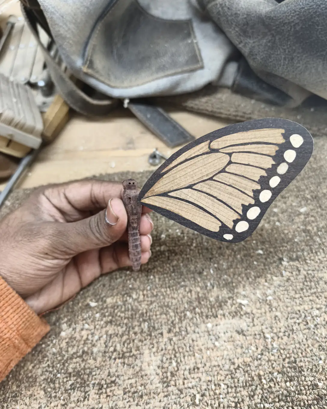 A hand holds up one finished wing over a sawdust-covered floor, the black ebony border and white maple spots complete.